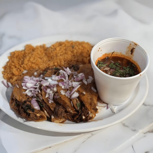 Mexican birria tacos topped with red onions, a side of rice, and a cup of consommé.