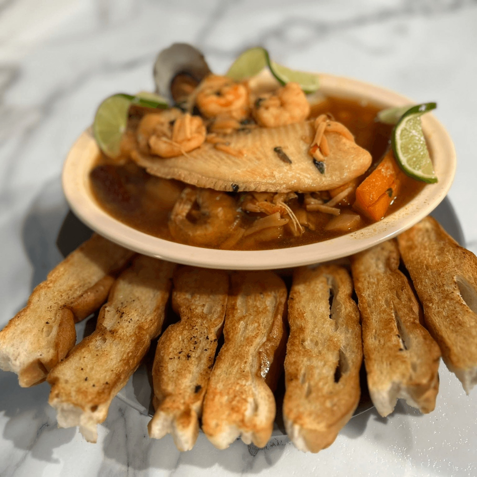 Mexican seafood soup with fish, shrimp, and vegetables, garnished with lime, served with toasted bread.