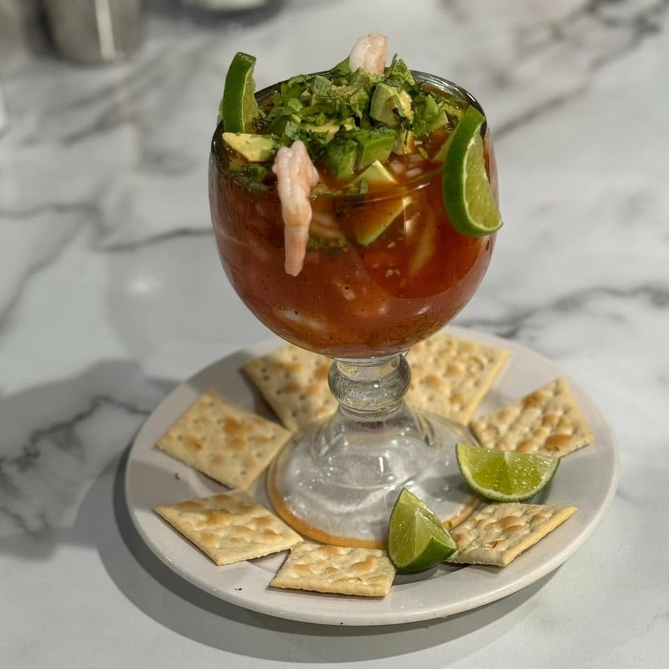 Mexican shrimp cocktail with avocado, cilantro, and lime, served with crackers on a white plate.