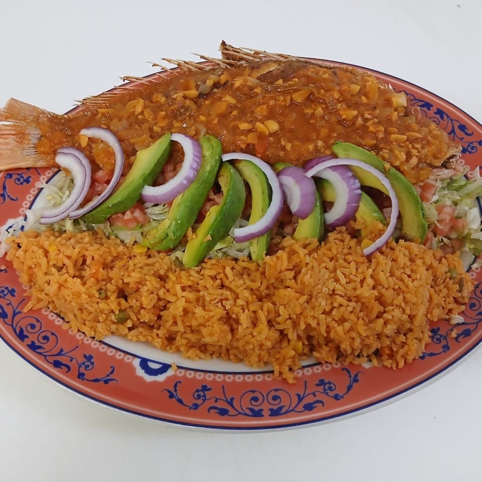 Whole fried fish topped with sauce, avocado, red onion, and rice on a decorative plate.