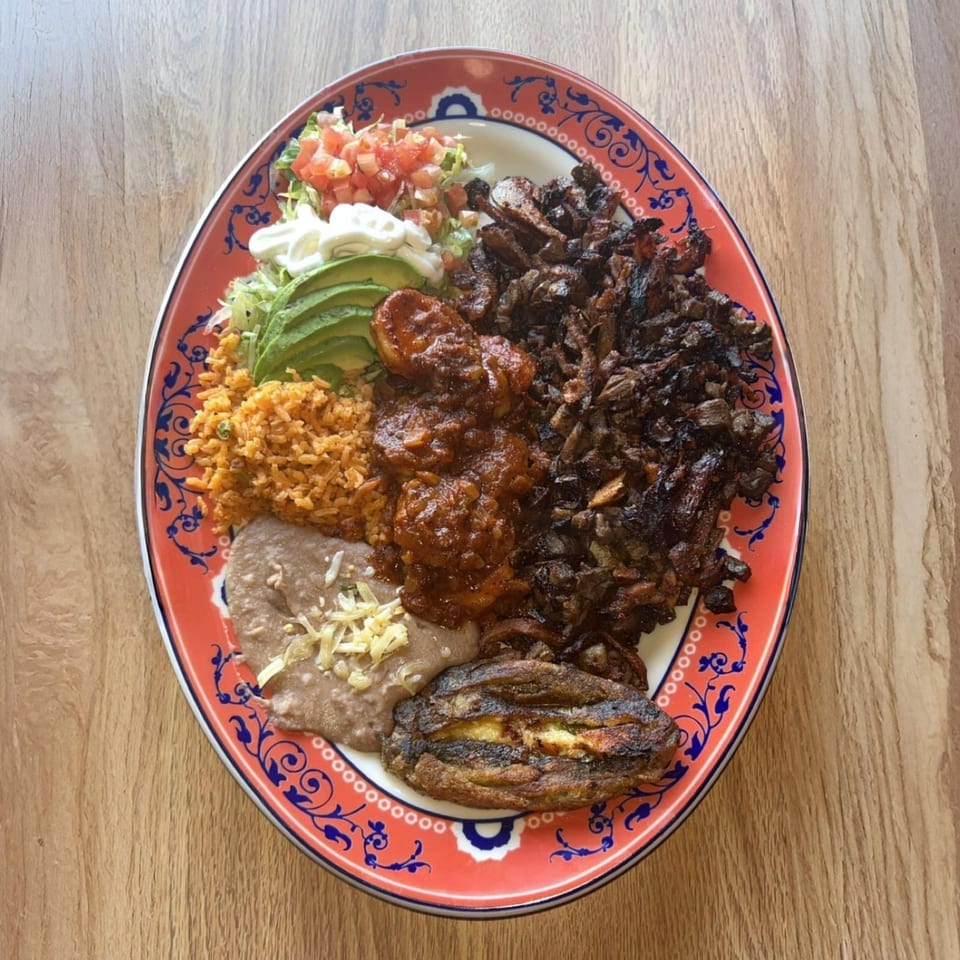 A vibrant Mexican platter with rice, beans, avocado, salsa, shrimp, and dark meat on a red plate.